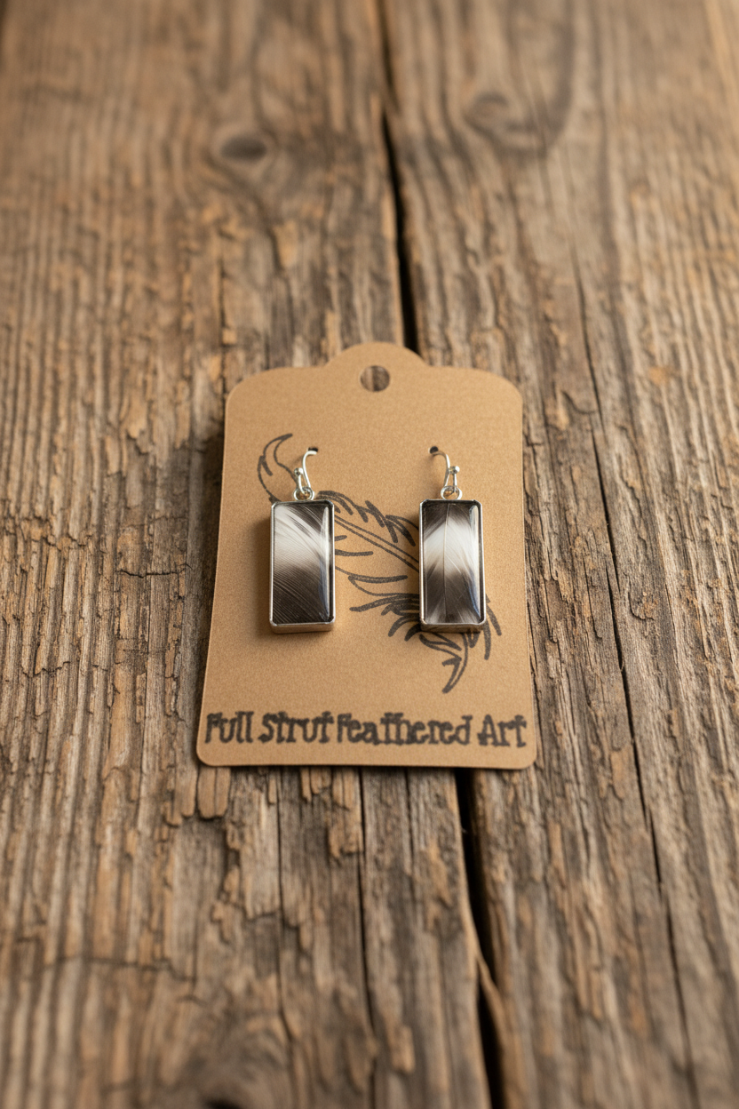 Black and white feather rectangle earrings with silver bezel on rustic wood background